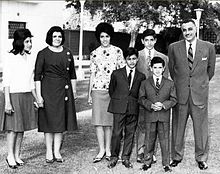 Groupe familial prenant la pose dans un jardin. Nasser et ses fils portent des costumes et son épouse et ses filles portent des chemises et des jupes longues.