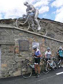 Photographie montrant trois cyclistes faisant une pause au pied d'une statue en métal.