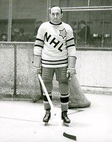 Photo de Morenz devant un but dans un chandail blanc marqué des lettres NHL.