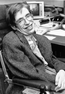 Photographie en noir et blanc d'un homme à la tête penchée et avec des lunettes, souriant.